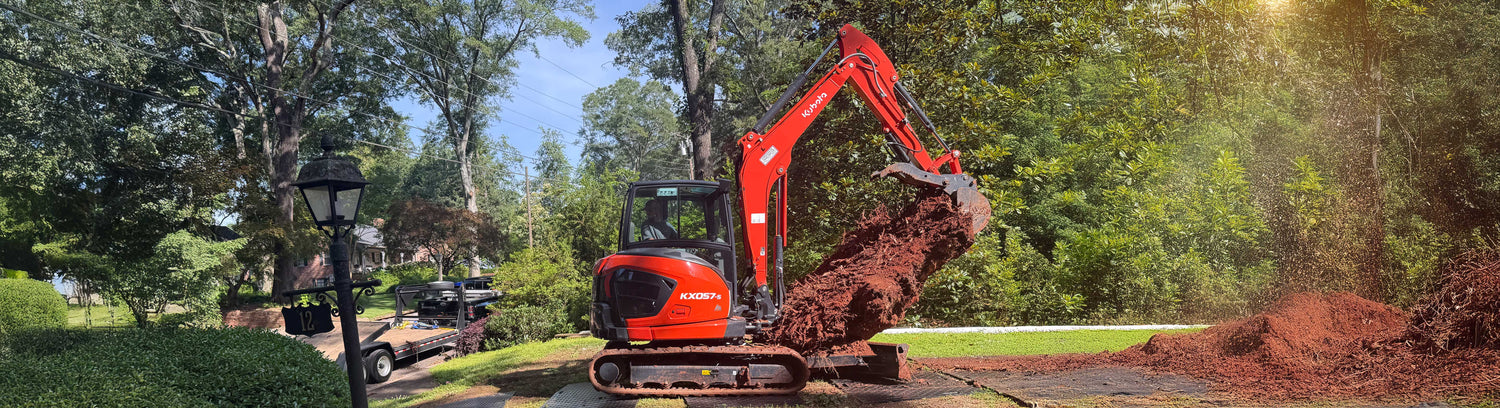 Orange excavator digging in a garden with trees and a truck in the background