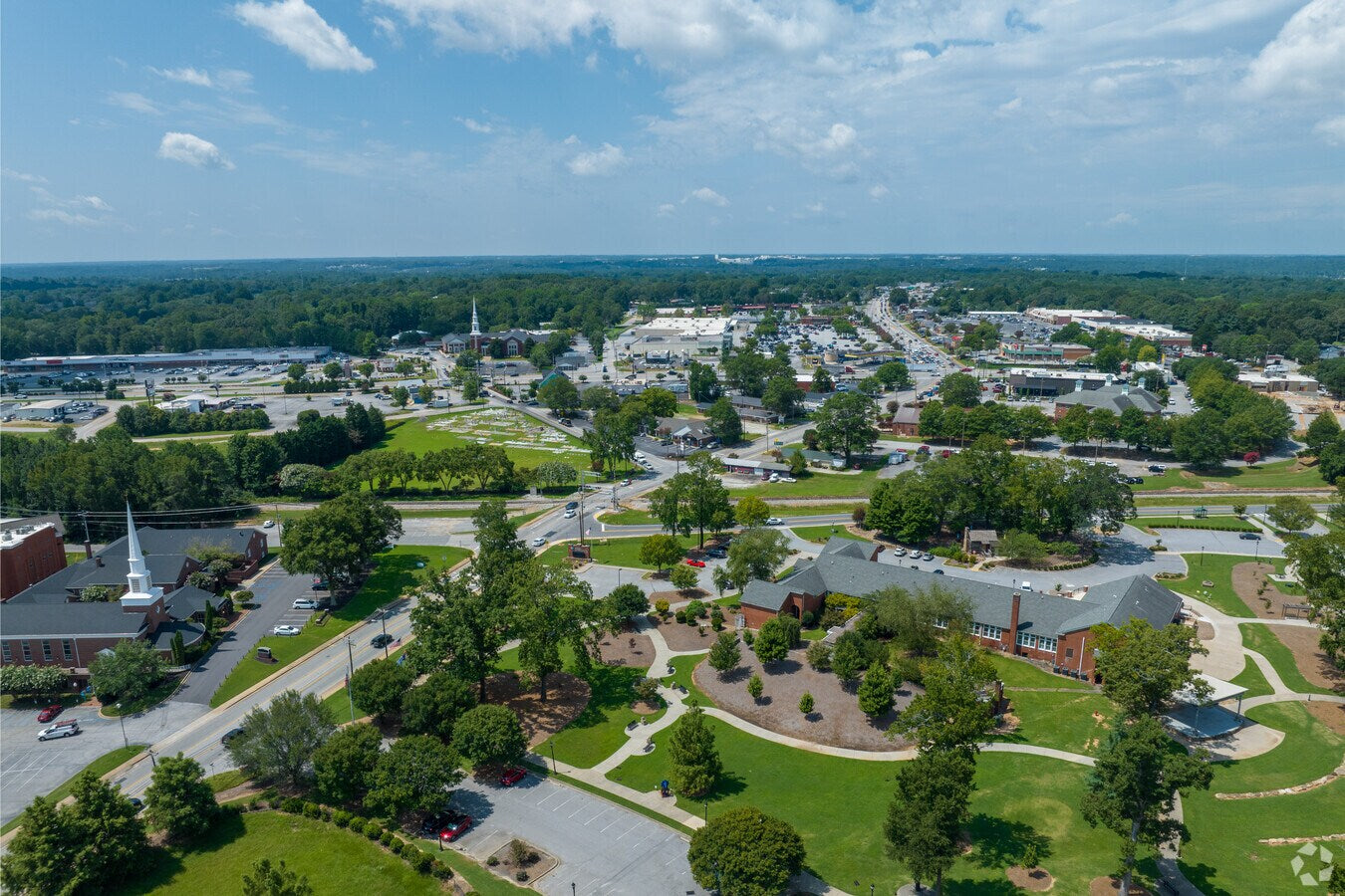 Aerial view of a small town with roads, buildings, and green spaces under a blue sky.