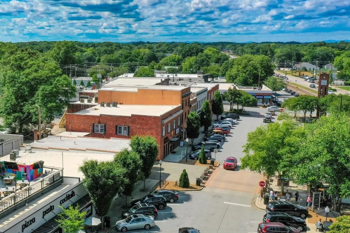 Aerial view of a small town with buildings, cars, and greenery under a blue sky.