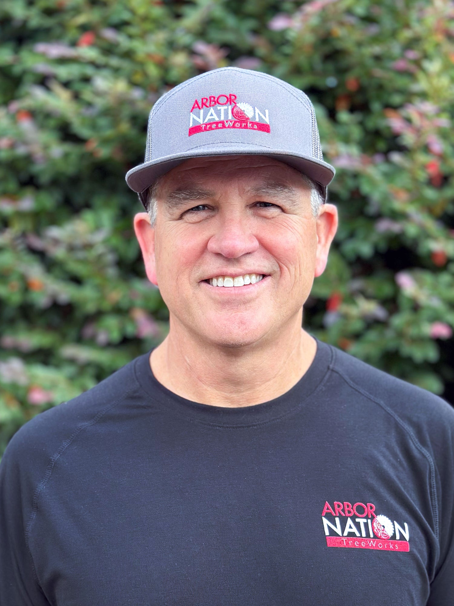Man wearing a gray cap and black shirt with 'Arbor Nation' logo in front of green foliage.