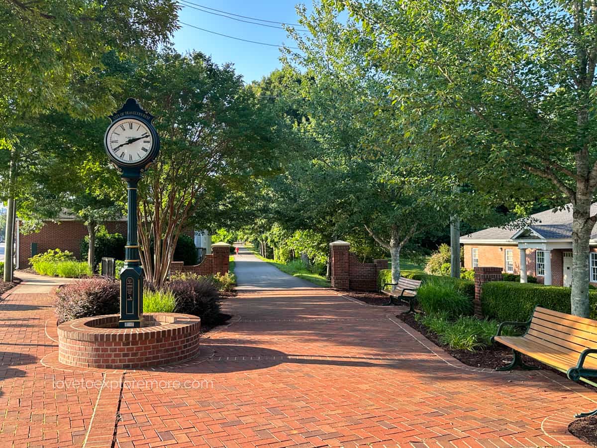 Paved walkway with a clock tower and bench in a park-like setting